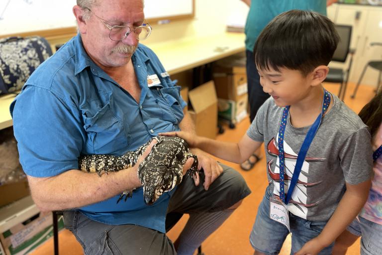 Young boy petting a snake that is being held by a man.