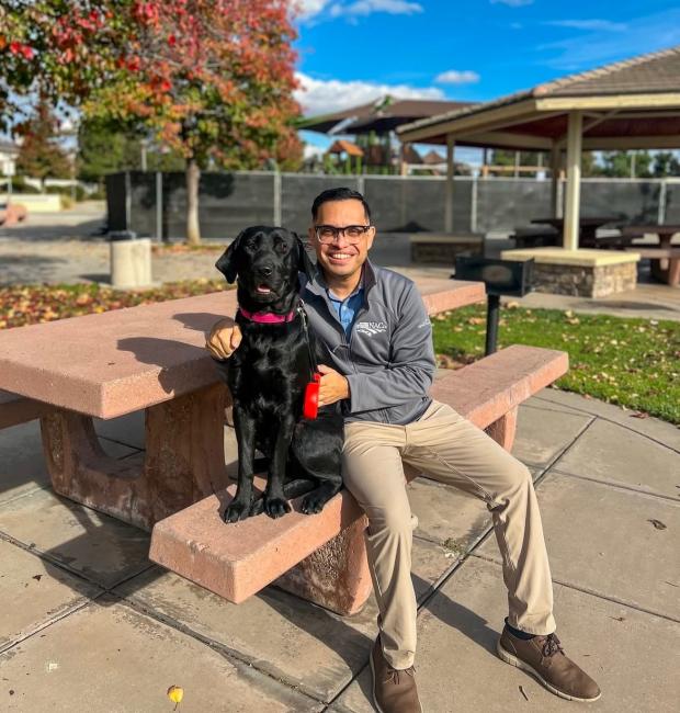 A man is sitting on a bench. A large black dog sits next to him.