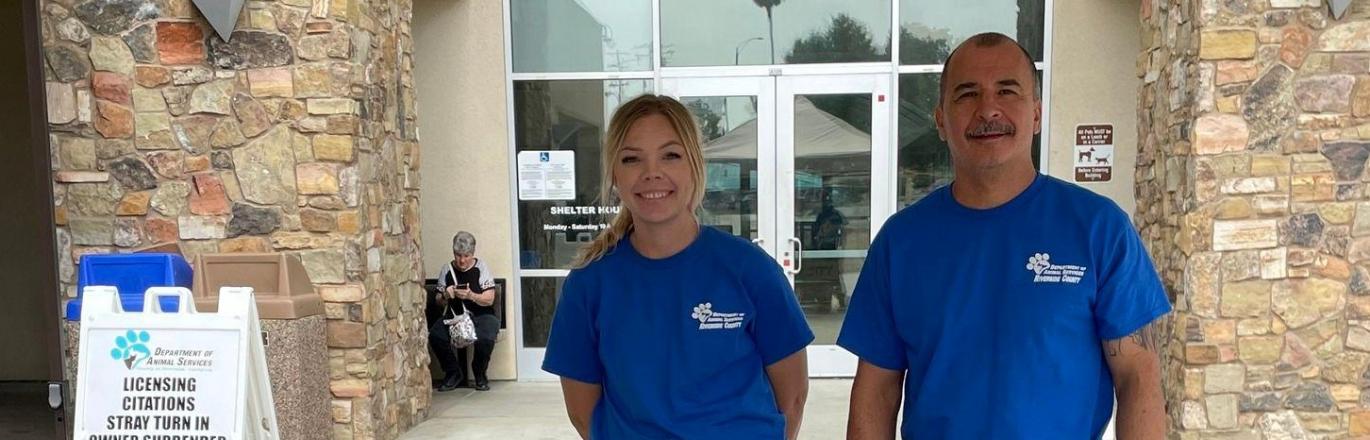 Two Department of Animal Services Staff Members standing behind pet support table outside the front of the Western Riverside County/City Animal Shelter