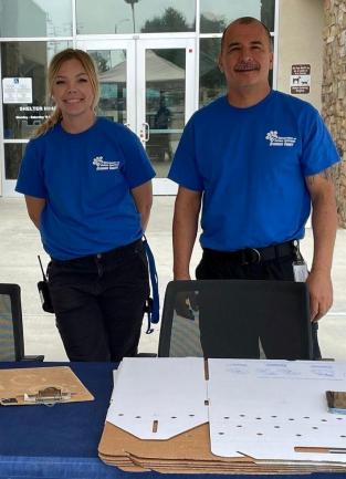Two Department of Animal Services Staff Members standing behind pet support table outside the front of the Western Riverside County/City Animal Shelter