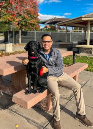 A man is sitting on a bench. A large black dog sits next to him.